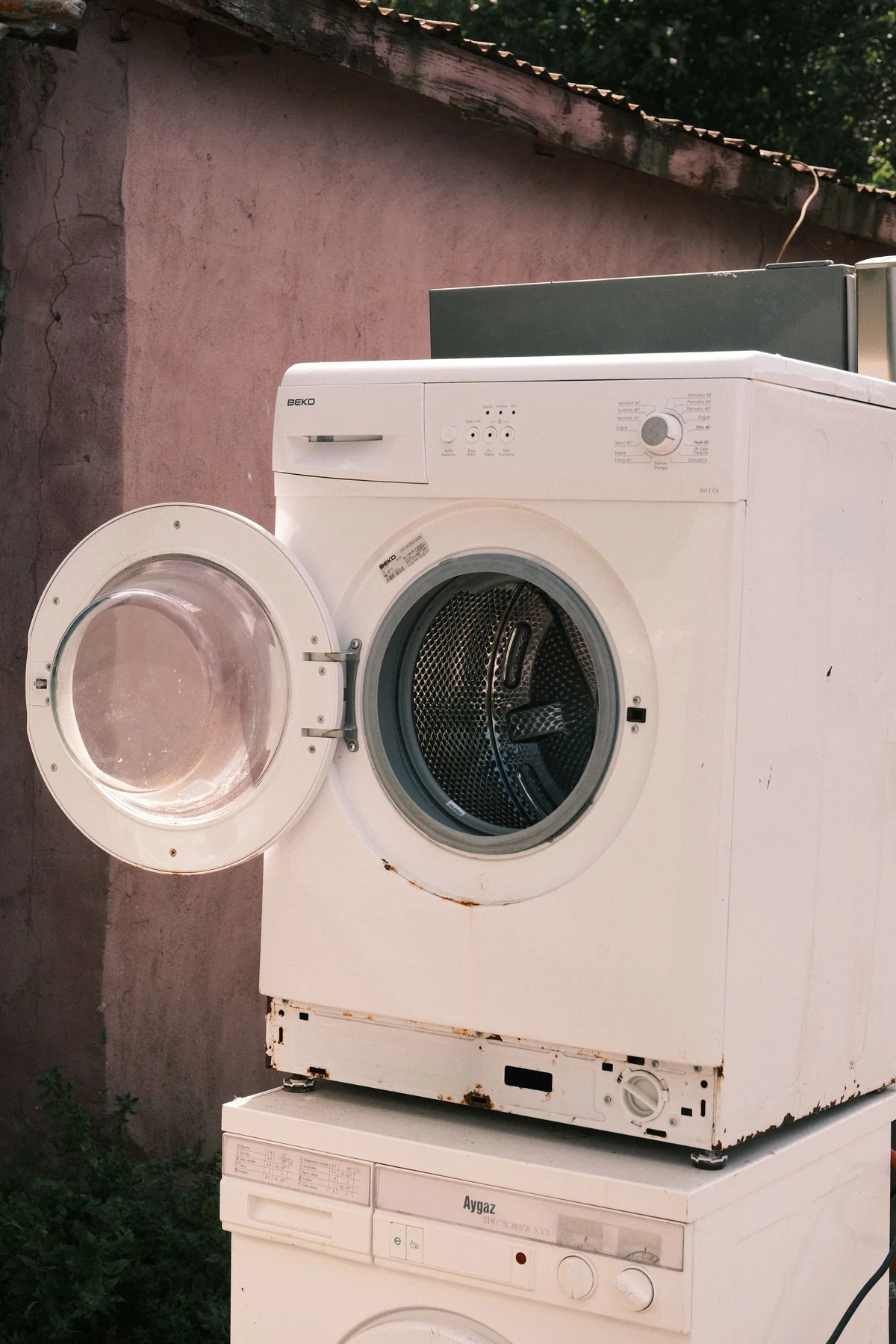 A pair of old front-load washing machines set outdoors for pickup